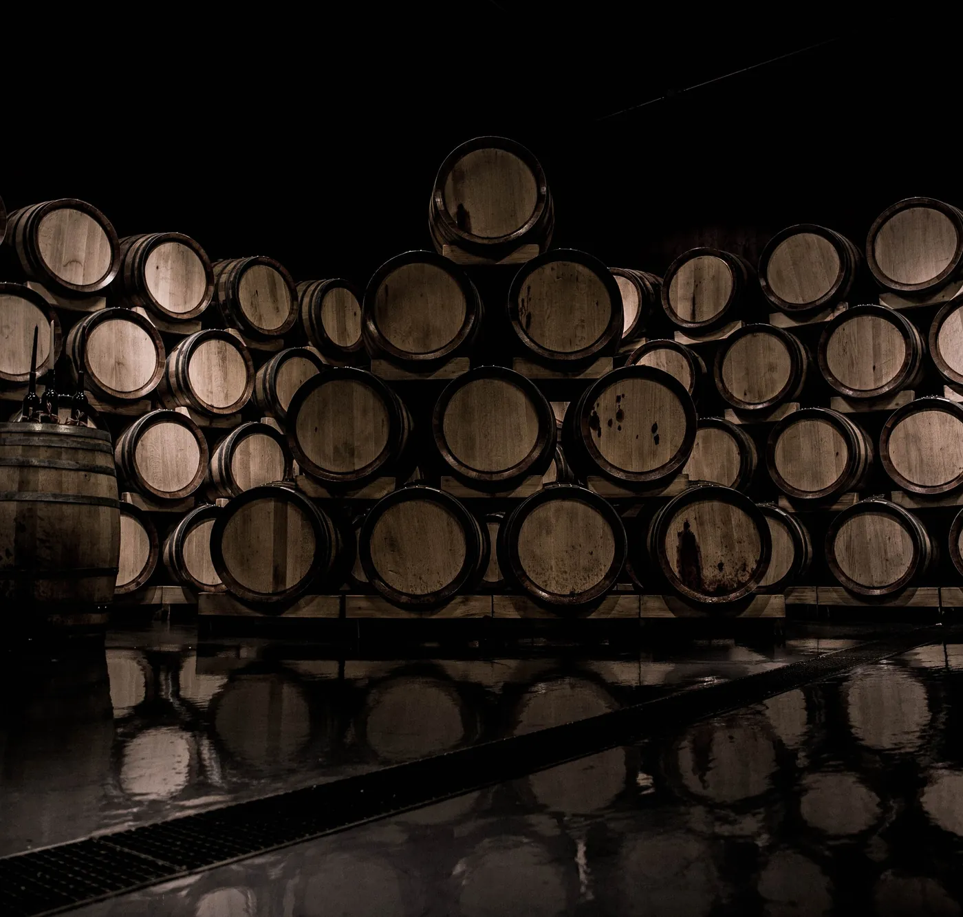 Casks racked in a dark bonded warehouse, reflected in the wet floor